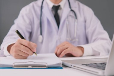 Hasta bakımı için reçete yazan beyaz önlüklü bir erkek doktor, sağlık ve tedaviyi vurgulayan bir hastane geçmişine sahip..