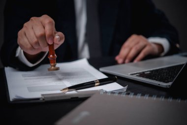 Ofisteki bir adam resmi bir belgeyi kauçuk mühür ile damgalar. Otoriteyi sembolize eder ve yasal evrak işlemlerinde onay verir. Sözleşmeler veya sertifikalar gibi..