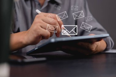 Modern iş çözümlerinde yüzen e-posta simgeleri, dijital iletişimi, haber bülteni çevrimiçi mesajlaşmayı ve e-posta pazarlama bilgilerini temsil eden bir tablet üzerinde bir stil kullanan bir işadamı.