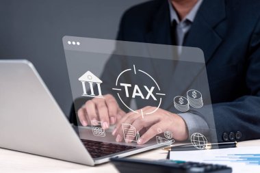 Hesap makinesi ve dizüstü bilgisayar kullanarak vergi hesaplamalarında çalışan bir finans uzmanı. Belgeler, para birimi ve vergi işlemini temsil eden bir banka binası gibi çevrimiçi vergiler sergileniyor.