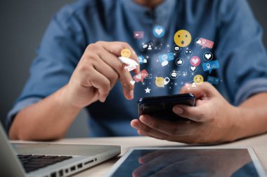 Sosyal medya simgelerinin yüzdüğü bir akıllı telefon kullanan işadamı, dijital pazarlamayı ve çevrimiçi iletişimi temsil ediyor.