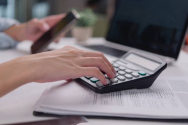 Ofis çalışanı hesap makinesi ve akıllı telefonla iş verilerini ya da mali raporları analiz ederek hesaplamalar yapıyor..