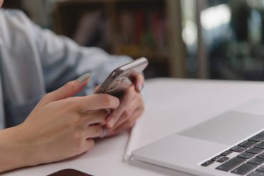 Akıllı bir telefonla dizüstü bilgisayarda yazı yazan bir kişinin yakın çekim görüntüsü, günlük hayatta mobil ve dijital teknolojinin karışımını temsil ediyor..