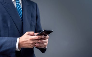 Modern bir profesyonel ortamda dijital iletişim için akıllı telefon kullanan bir iş adamı. Görüntü mobil teknoloji ve iş bağlantısını yansıtıyor.