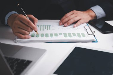 İşadamı masasında bir kalemle mali raporları ve grafikleri analiz ediyor ve büyüme verilerine odaklanıyor..