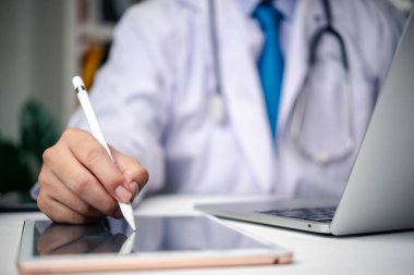 Close-up of a medical professional working on a tablet with a stylus, wearing a stethoscope, and using technology for patient care.