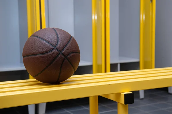 Brown basketball ball on yellow bench in locker room. Horizontal sport poster, greeting cards, headers, website