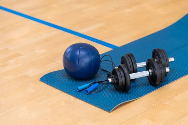 Dumbbells, medicine ball and gym mat on wooden surface. Concept of rehabilitation and sport training equipment