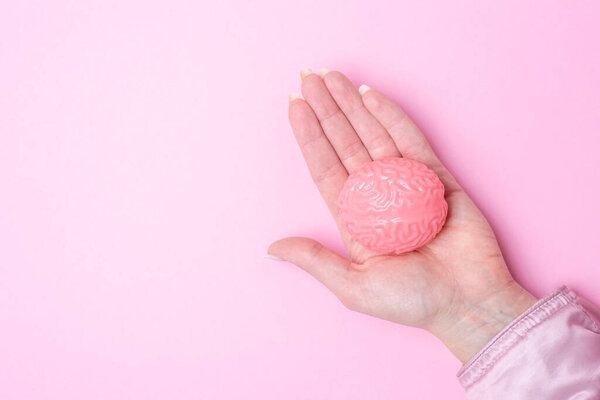 Hand holding pink brain isolated on pink background