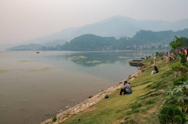 Pokhara, Nepal: 14 Nisan 2023 - Pokhara şehrindeki Phewa Gölü çevresindeki birçok yerel sakinin dinlendiği ve göl kenti faaliyetlerinin keyfini çıkardığı bir manzara.