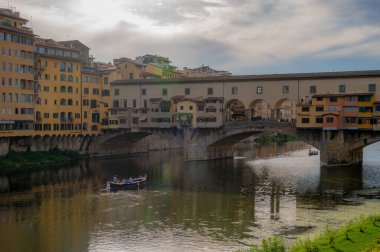 Floransa, İtalya - 8 Ağustos 2023: Tarihi Ponte Vecchio köprüsü ve İtalya 'nın Floransa kentinde küçük bir kayık geçidi bulunan Arno Nehri' nin huzurlu manzarası. Sudaki canlı yansımalar resim gibi bir sahne yaratır..