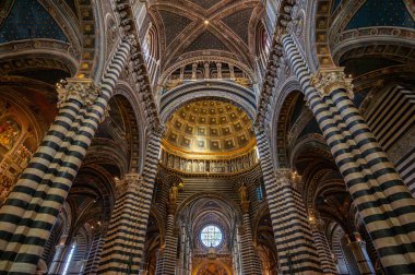 Siena, İtalya - 9 Ağustos 2023: Siena Katedrali 'nin nefes kesici iç manzarası, çizgili kolonları, yüksek tavanları ve karmaşık mermer döşeme tasarımları sergilenmektedir..