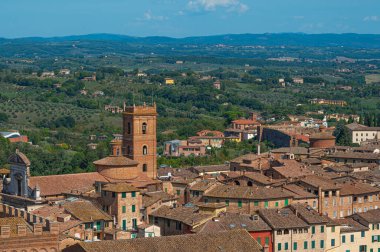 Terasotta çatıları, ortaçağ mimarisi ve açık mavi gökyüzünün altında yuvarlanan tepelerin yer aldığı tarihi İtalyan şehri Siena 'nın panoramik bir görüntüsü..