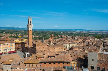 Terasotta çatıları, ortaçağ mimarisi ve açık mavi gökyüzünün altında yuvarlanan tepelerin yer aldığı tarihi İtalyan şehri Siena 'nın panoramik bir görüntüsü..