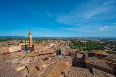 Terasotta çatıları, ortaçağ mimarisi ve açık mavi gökyüzünün altında yuvarlanan tepelerin yer aldığı tarihi İtalyan şehri Siena 'nın panoramik bir görüntüsü..