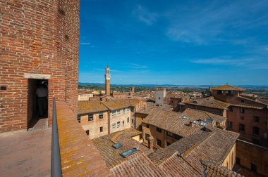 Terasotta çatıları, ortaçağ mimarisi ve açık mavi gökyüzünün altında yuvarlanan tepelerin yer aldığı tarihi İtalyan şehri Siena 'nın panoramik bir görüntüsü..