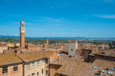Terasotta çatıları, ortaçağ mimarisi ve açık mavi gökyüzünün altında yuvarlanan tepelerin yer aldığı tarihi İtalyan şehri Siena 'nın panoramik bir görüntüsü..
