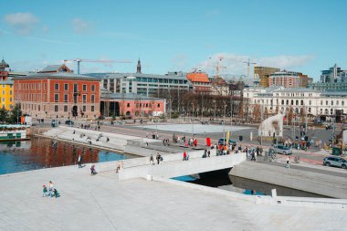 Oslo, Norveç - 13 Nisan 2024: İnsanlar Oslo Opera Binası 'nda yürüyor ve dinleniyor, liman kenarında eğimli çatısı olan modern bir mimari yapı..