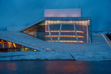Oslo Opera Binası 'nın manzarası. Etrafta yürüyen ve rahatlayan insanlar var. Sahne alacakaranlıkta çekilmiştir..