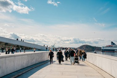 Oslo, Norveç - 13 Nisan 2024: İnsanlar Oslo Opera Binası 'nda yürüyor ve dinleniyor, liman kenarında eğimli çatısı olan modern bir mimari yapı..
