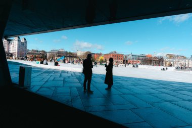 Oslo, Norveç - 13 Nisan 2024: İnsanlar Oslo Opera Binası 'nda yürüyor ve dinleniyor, liman kenarında eğimli çatısı olan modern bir mimari yapı..