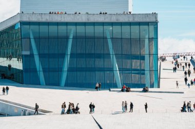 Oslo, Norveç - 13 Nisan 2024: İnsanlar Oslo Opera Binası 'nda yürüyor ve dinleniyor, liman kenarında eğimli çatısı olan modern bir mimari yapı..