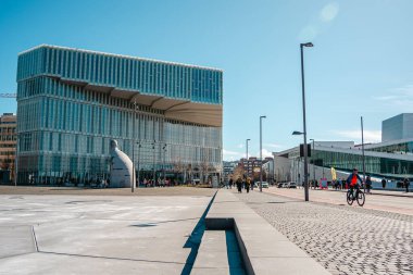 Oslo, Norveç - 13 Nisan 2024: İnsanlar Oslo Opera Binası 'nda yürüyor ve dinleniyor, liman kenarında eğimli çatısı olan modern bir mimari yapı..