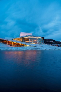 Oslo Opera Binası 'nın manzarası. Etrafta yürüyen ve rahatlayan insanlar var. Sahne alacakaranlıkta çekilmiştir..