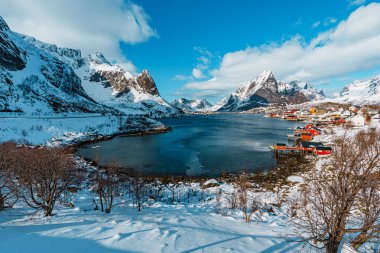 Fiyort boyunca renkli evlerin yer aldığı karlı bir manzara, Reine, Lofoten 'in arka planında görkemli dağlar var..