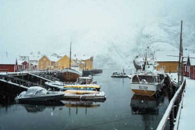Nusfjord, Norveç - 7 Nisan 2024: Bir kış manzarasında fiyort tarafından karla kaplı renkli bir köy. Lofoten Adası.