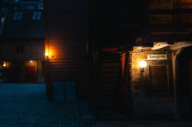 Norveç, Bergen 'deki Bryggen İskelesi' nden atmosferik gece sahneleri, rahat dükkanları, aydınlık sokakları ve sıcak ışıklandırmadaki ahşap tarihi binaları gösteriyor..