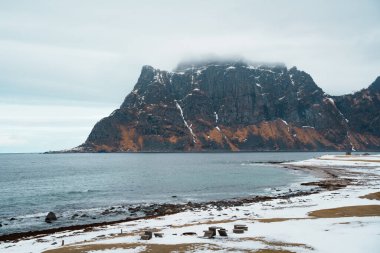 Norveç 'in Lofoten kentindeki Uttakleiv Sahili' nde engebeli kayalar, okyanus dalgaları ve karlı dağ arka planının yer aldığı dramatik kutup sahneleri.