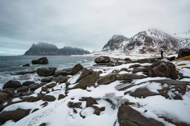 Norveç 'in Lofoten kentindeki Uttakleiv Sahili' nde engebeli kayalar, okyanus dalgaları ve karlı dağ arka planının yer aldığı dramatik kutup sahneleri.
