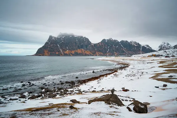 Norveç 'in Lofoten kentindeki Uttakleiv Sahili' nde engebeli kayalar, okyanus dalgaları ve karlı dağ arka planının yer aldığı dramatik kutup sahneleri.