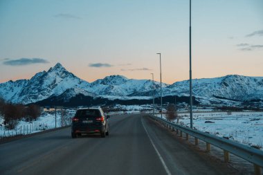 Lofoten, Norveç 'teki Leknes' in göz kamaştırıcı kış manzaraları, karla kaplı dağlar, sakin su yansımaları ve gün batımında kıyı yolları yer alıyor..