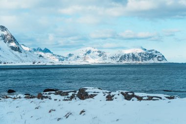 Norveç 'in Lofoten kentindeki yol manzarasında karla kaplı dramatik dağlar ve Arktik fiyort yer alıyor..