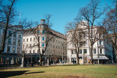 Oslo, Norveç - 13 Nisan 2024: Oslo Katedrali ve yakınlarındaki klasik binaların güneşli manzarası, Norveç 'in canlı kentsel yaşamını ve tarihsel cazibesini yansıtıyor.