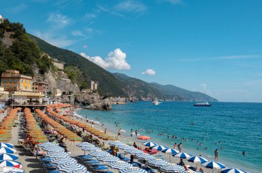 Cinque Terre, İtalya - 7 Eylül 2022: Monterosso Al Mare, İtalya 'da kalabalık plaj, renkli şemsiyeler, yüzücüler ve manzaralı Ligurian kıyı şeridini gösteriyor.