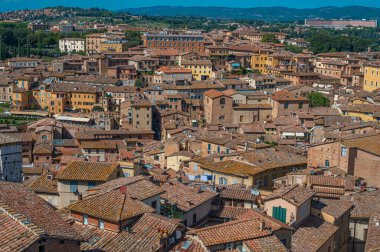 İtalya, Siena üzerinde panoramik manzara, arka planda yoğun terakotta çatıları, ortaçağ mimarisi ve manzaralı Toskana tepeleri sergileniyor.