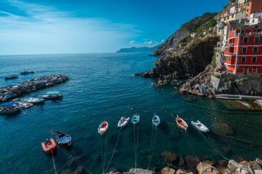 Riomaggiore, İtalya - 7 Şubat 2022: Renkli binalar, kayalık kayalıklar, turkuaz deniz, tekneler ve turistlerle Riomaggiore, Cinque Terre 'nin resimli sahnesi.