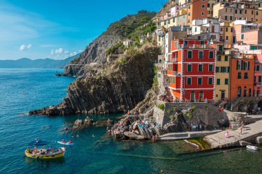 Riomaggiore, İtalya - 7 Şubat 2022: Renkli binalar, kayalık kayalıklar, turkuaz deniz, tekneler ve turistlerle Riomaggiore, Cinque Terre 'nin resimli sahnesi.