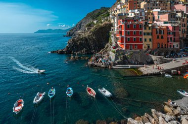 Riomaggiore, İtalya - 7 Şubat 2022: Renkli binalar, kayalık kayalıklar, turkuaz deniz, tekneler ve turistlerle Riomaggiore, Cinque Terre 'nin resimli sahnesi.