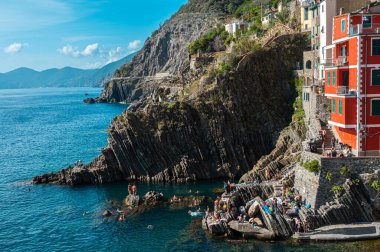 Riomaggiore, İtalya - 7 Şubat 2022: Renkli binalar, kayalık kayalıklar, turkuaz deniz, tekneler ve turistlerle Riomaggiore, Cinque Terre 'nin resimli sahnesi.