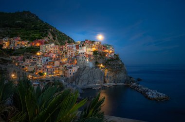 Mehtaplı bir gecede Manarola 'nın sihirli manzarası Cinque Terre' deki sakin Ligurian sularında parlayan köy ışıkları yansıyor..