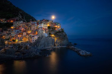 Mehtaplı bir gecede Manarola 'nın sihirli manzarası Cinque Terre' deki sakin Ligurian sularında parlayan köy ışıkları yansıyor..
