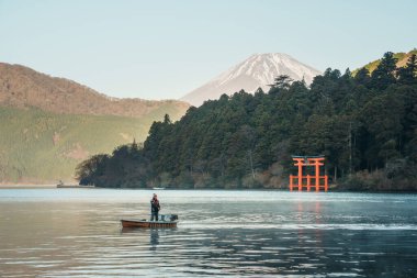 Hakone, Japonya - 10 Aralık 2023: Fuji Dağı ve Hakone, Japonya 'daki sık orman tarafından çerçevelenmiş ikonik torii kapısı ile Ashi Gölü' nde sabah tekne gezisi. Tori kapısındaki Japonca metin 