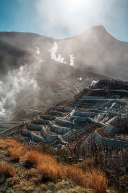 Hakone, Japonya 'da Owakudani' nin dramatik jeotermal manzarası, yükselen buhar bacaları, engebeli arazi ve manzaralı bir halat gezisi.
