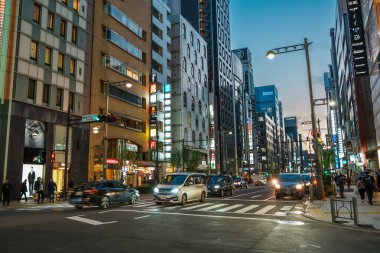 Tokyo, Japonya - 15 Aralık 2023: Ginza, Tokyo 'da kalabalık cadde, alacakaranlıkta, arabalar, yayalar ve aydınlık binalarla.