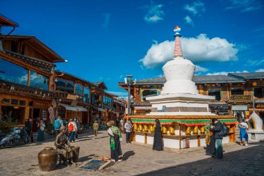 Shangri-La, Çin - 20 Ekim 2024 Dukezong Antik Kenti 'nin hareketli meydanında altın dua tekerleriyle önde gelen beyaz bir stupa duruyor..