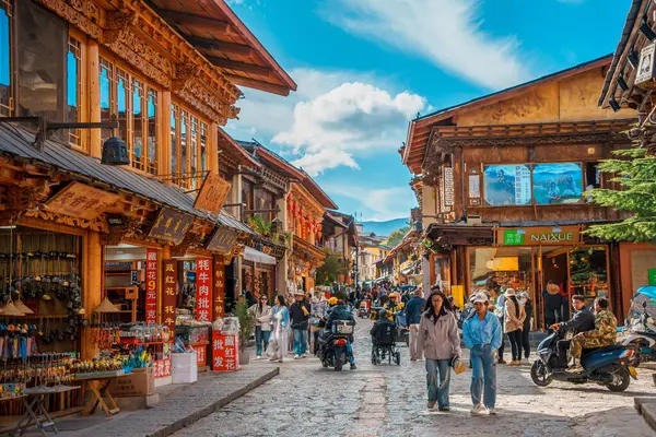Shangri-La, Çin - 20 Ekim 2024 Dukezong Antik Kasabası 'nda canlı bir cadde geleneksel ahşap binalar ve parlak bir gökyüzünün altındaki dükkanlarla dolu..